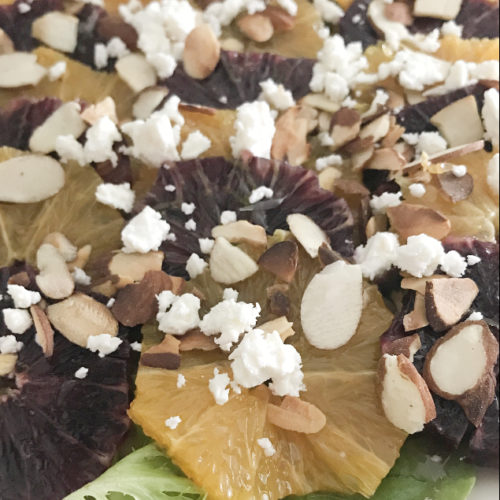 Oranges on a bed of lettuce topped with sliced almonds and feta