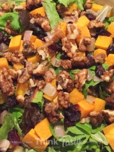 Salad topped with butternut squash, dried cranberries, and spiced walnuts