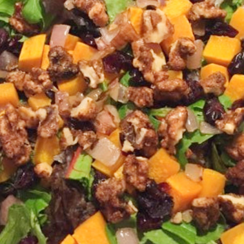 Salad topped with butternut squash, dried cranberries, and spiced walnuts